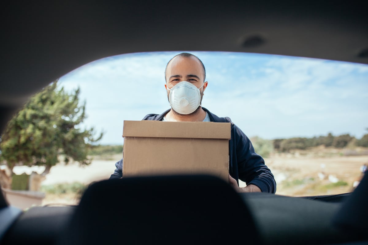 Man carrying box from his car, wearing protection mask
