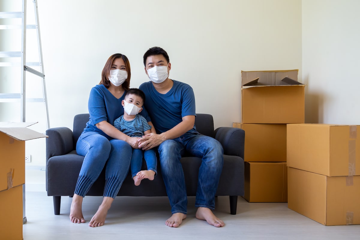 Asian family wearing protective medical mask for prevent virus covid-19 during moving day and relocating at new home. Moving house and new real estate concept