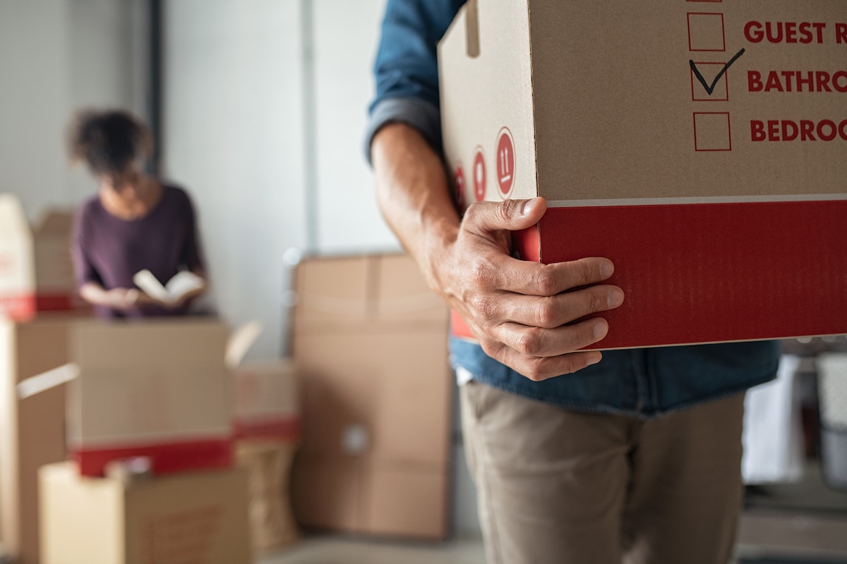 Closeup of man holding cardboard at new home. Young man unpacking boxes in new apartment. Man hand carrying carton box while relocating with his girlfriend.